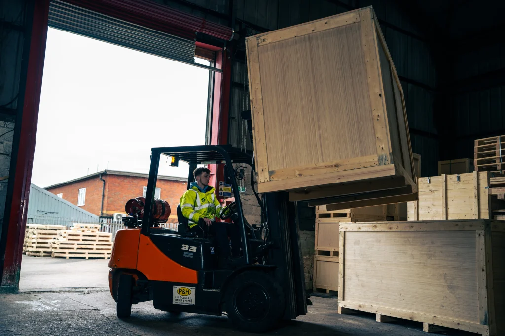 Forklift loading large MPAS‑compliant timber crates in an industrial warehouse, illustrating aerospace and defence packaging built to Military Packager Approval Scheme standards.
