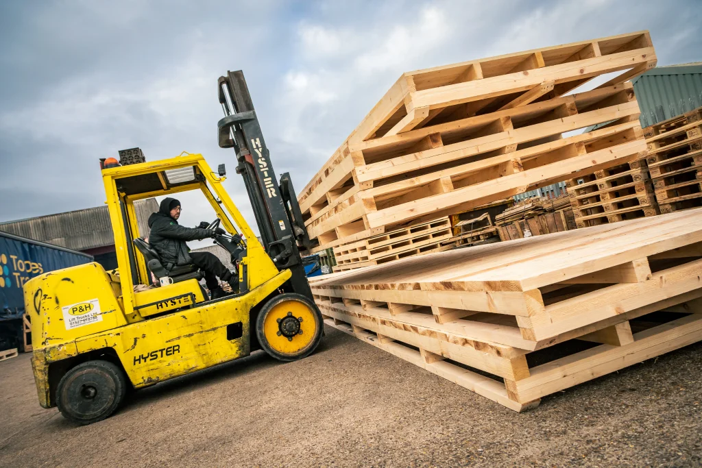 Forklift handling stacked timber skids and pallets at IM Export Services.
